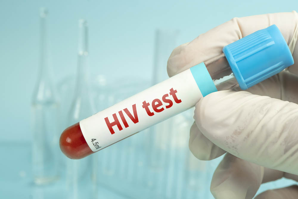 Hand holding blood sample for HIV test on a blue laboratory background.