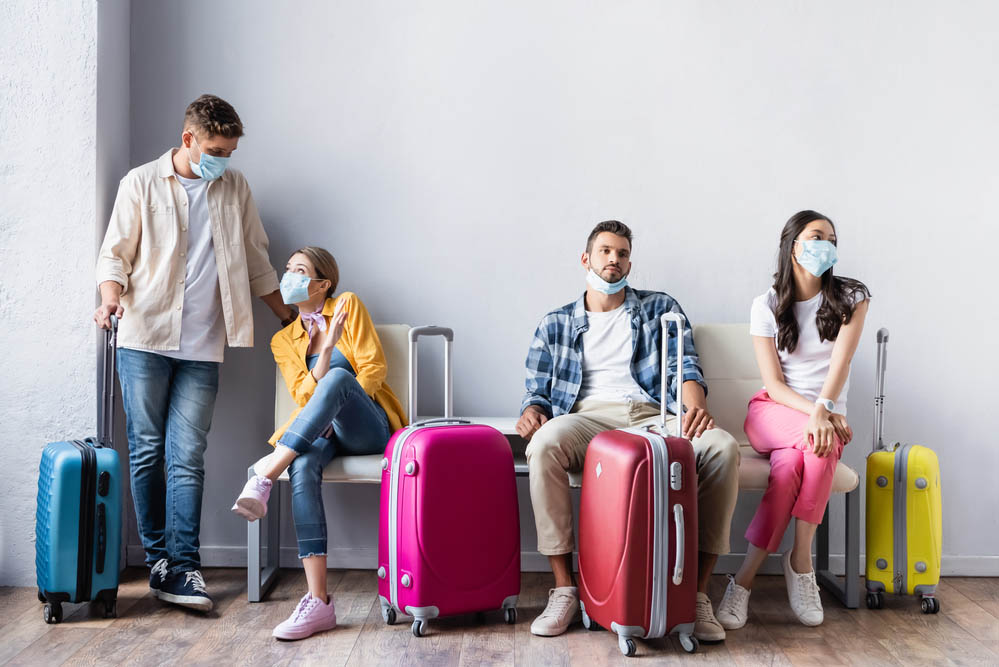Multicultural people in medical masks waiting near suitcases