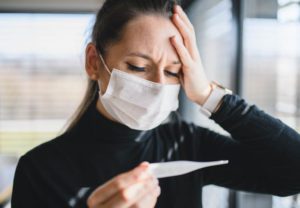 Worried woman in pain with thermometer and face masks indoors at home, Corona virus concept.
