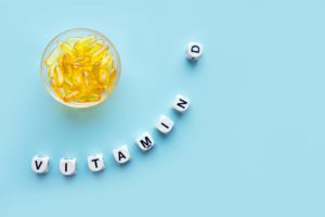 Yellow capsules in the round glass bowl and the word vitamin D from white cubes with letters on a blue background. VITAMIN D word for healthy and medical concept. Sunshine vitamin health benefits
