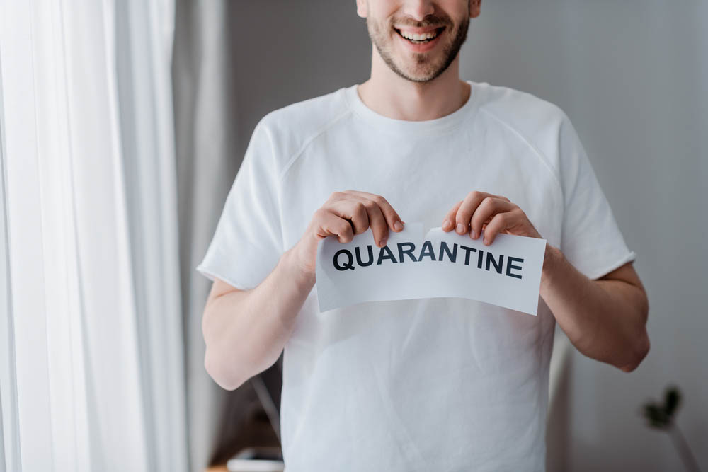 Cropped view of happy man ripping paper with quarantine lettering