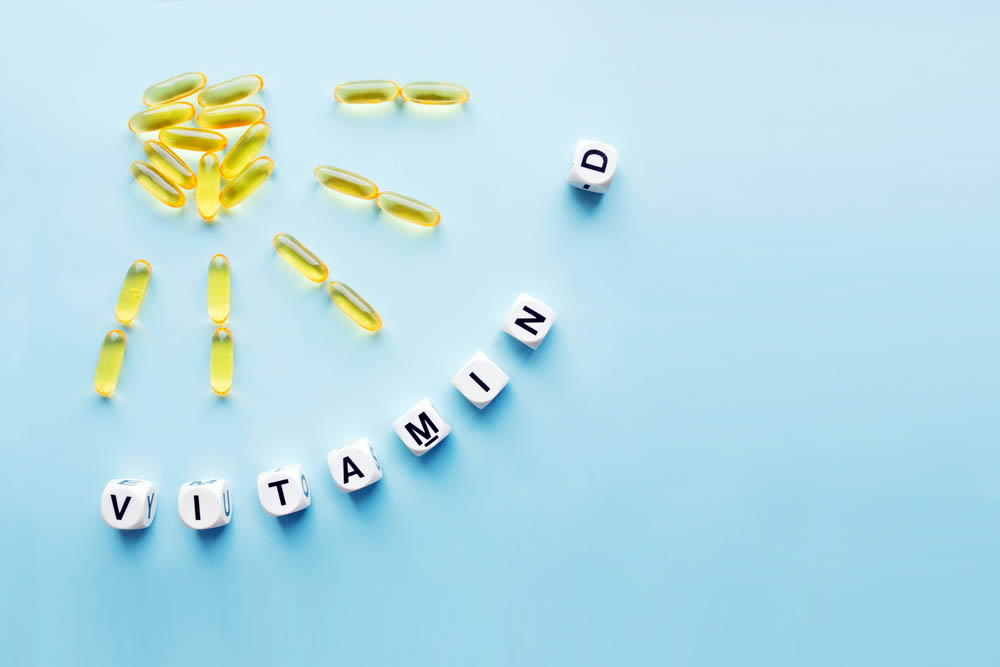 Yellow capsules in the form of the sun with rays and the word vitamin D from white cubes with letters on a blue background. VITAMIN D word for healthy and medical concept. Sunshine vitamin health benefits
