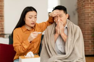 Loving young asian wife taking care of her sick husband, checking fever with thermometer