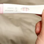 Positive pregnancy test held in hand.