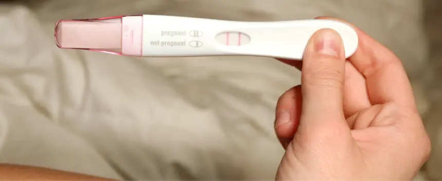 Positive pregnancy test held in hand.